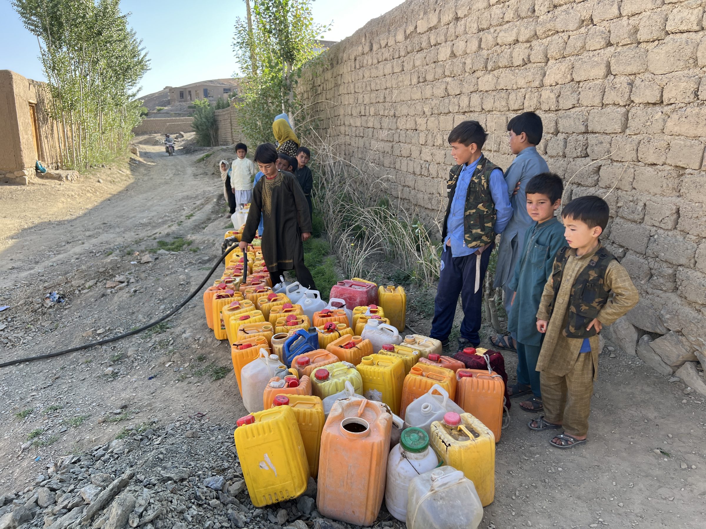 Children beside dozens of colorful water jerrycans in Ghor